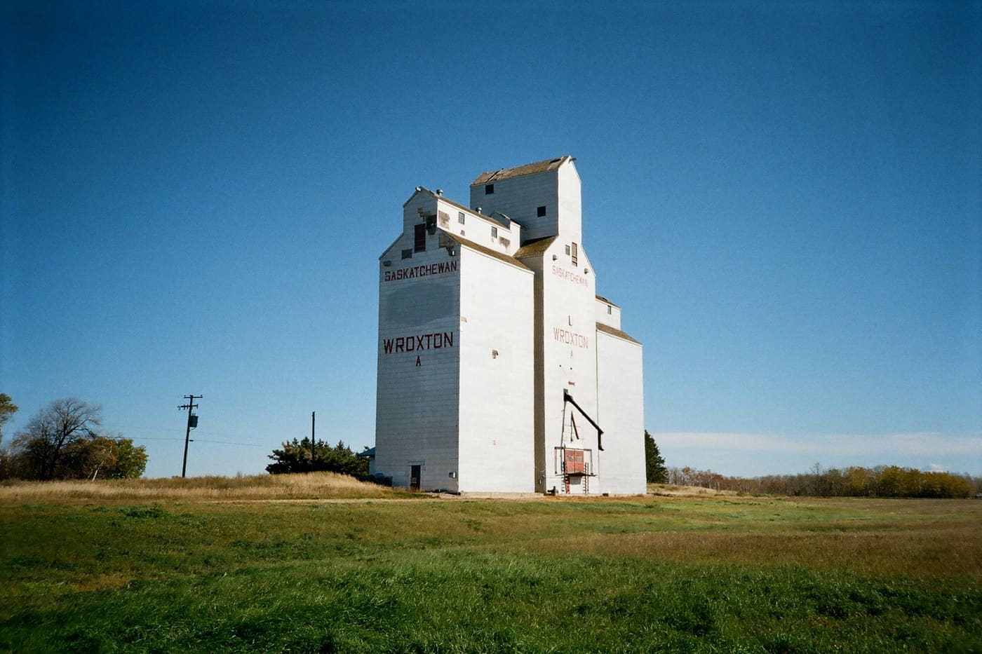 A white grain elevator beside a green field under a deep blue sky.