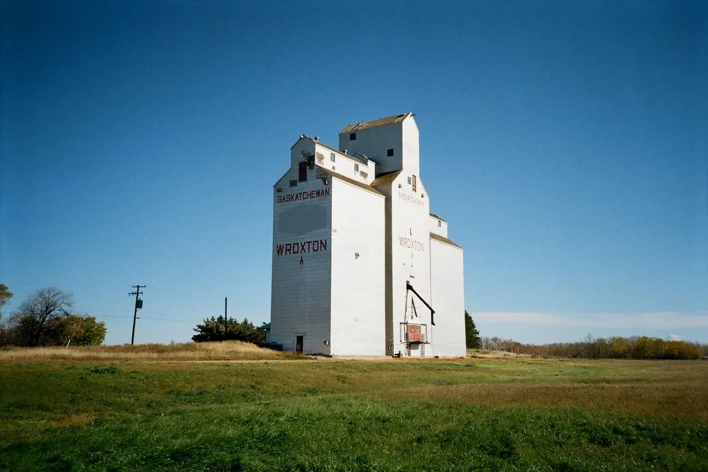 A white grain elevator beside a green field under a deep blue sky.