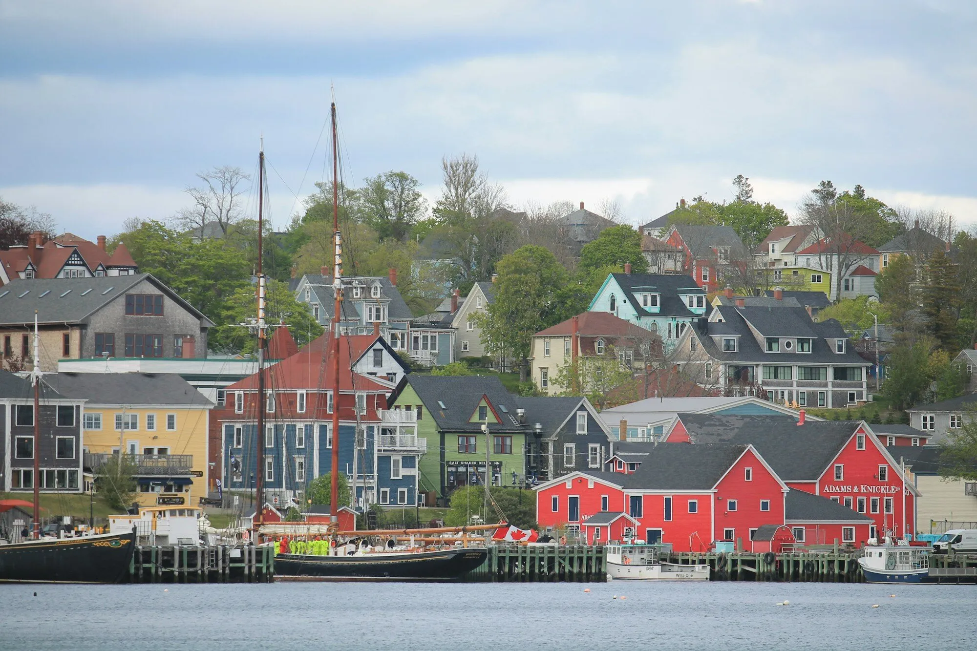 Colourful heritage buildings rise from the harbour in Lunenburg, Nova Scotia, with sailboats moored along the wharf.