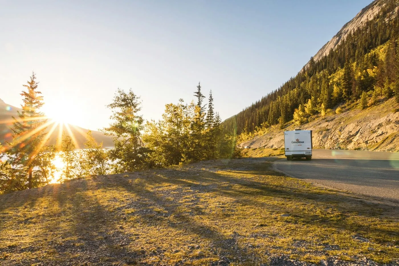 An RV driving a mountain highway at sunset, sunlight flaring through the trees.