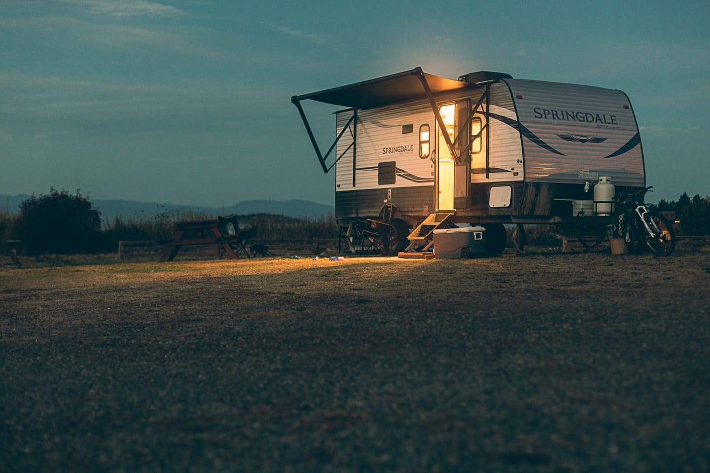 A small camper glowing in a field under a dark night sky.