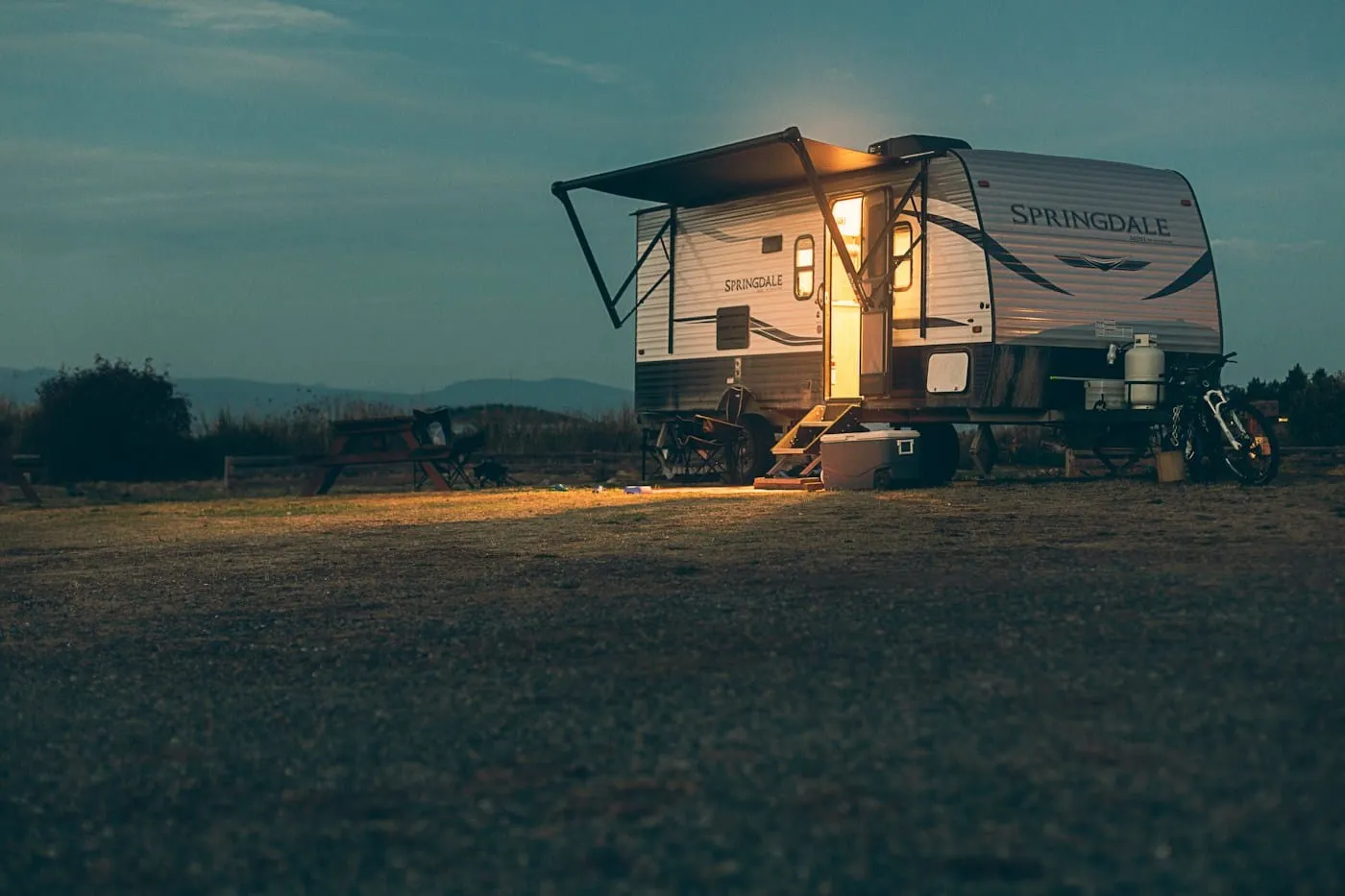 A small camper glowing in a field under a dark night sky.