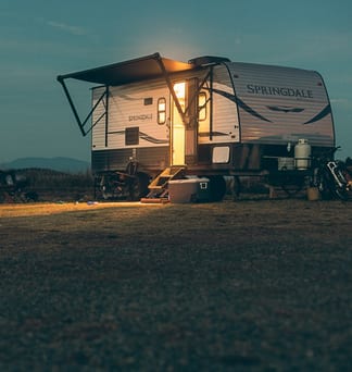 A small camper glowing in a field under a dark night sky.